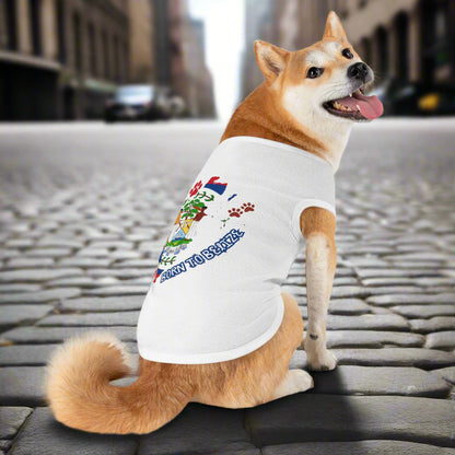 Dog wearing a white t-shirt with colorful graphics and text on a city street.